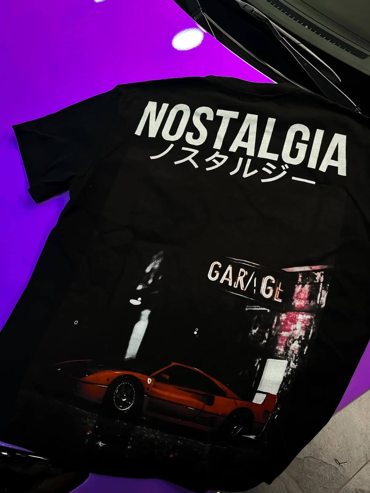 T-shirt UKIYO nera con la scritta “NOSTALGIA ノスタルジー” e la stampa di una Mazda RX-7 arancione.